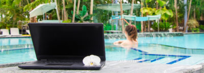 Frau in Whirlpool mit Laptop im Palmenparadies
