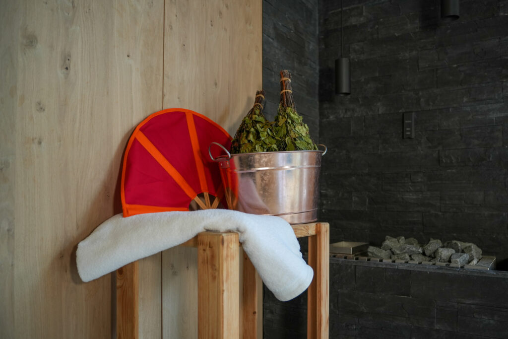 Aufguss-Utensilien: Birkenzweige, Fächer und Handtuch auf einem Tisch neben dem Saunaofen der Textilsauna Badeparadies Schwarzwald